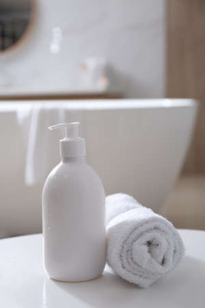 Bottle of shower gel and fresh towel on white table in bathroom