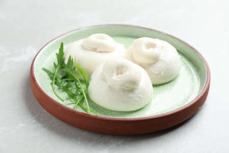 Delicious burrata cheese with arugula on light table, closeup