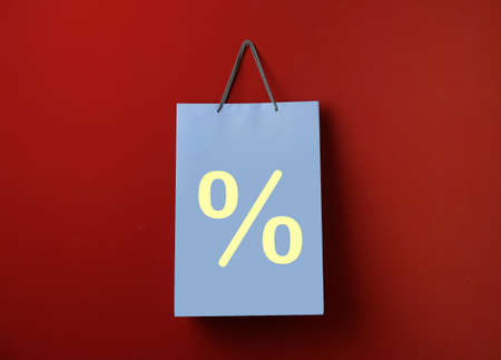 Light blue paper shopping bag with percent sign hanging on red wall. discount conceptの写真素材