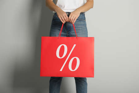Woman holding paper shopping bag with percent sign on light gray background, closeup. discount...
