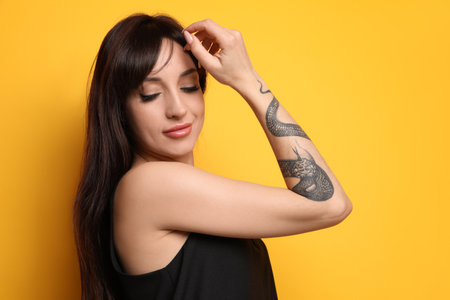 Beautiful woman with tattoos on arm against yellow backgroundの写真素材