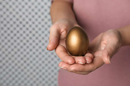 Woman holding golden egg on light background, closeup. Space for textの写真素材