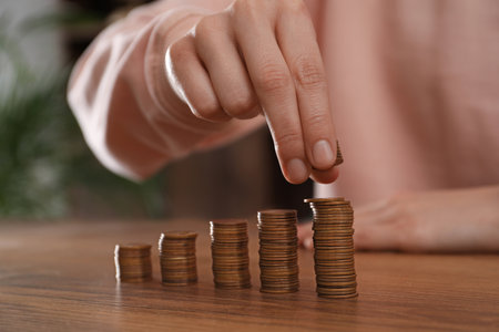 Woman stacking coins at wooden table indoors, closeup