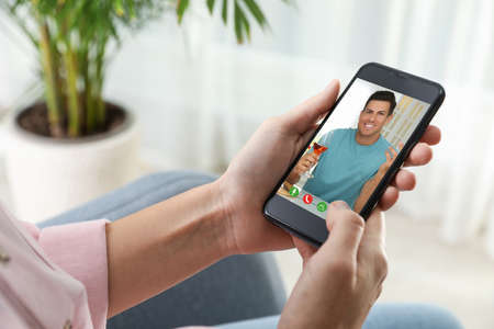 Woman talking with handsome man using video chat on smartphone indoors, closeup. Online dating