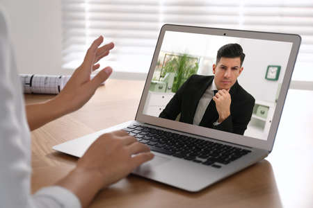 Woman talking with handsome man using video chat on laptop at wooden table, closeup. Online dating