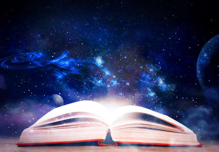 Wooden table with open book and beautiful universe on background