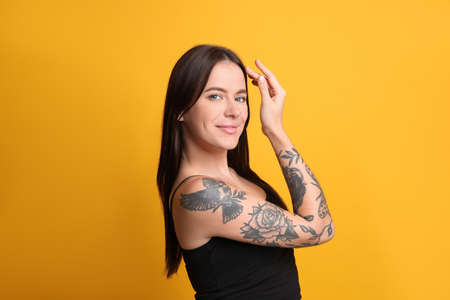 Beautiful woman with tattoos on arm against yellow backgroundの写真素材
