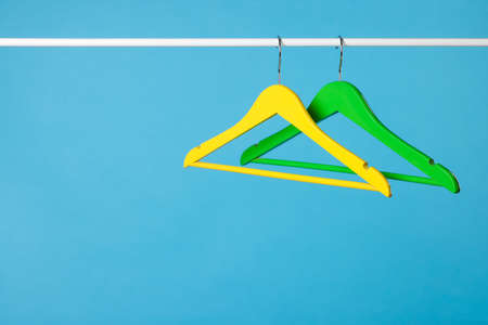 Bright clothes hangers on metal rail against light blue background. Space for textの写真素材