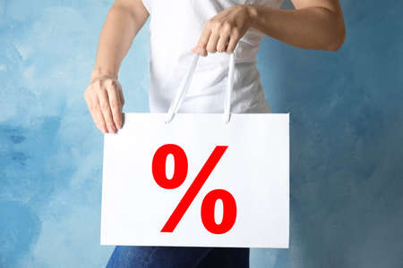 Woman holding paper shopping bag with percent sign near light blue wall, closeup. discount conceptの写真素材