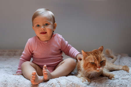 Adorable baby and cute red cat on bed indoorsの写真素材