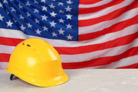 Yellow protective hard hat on light gray table against American flag. Space for textの写真素材