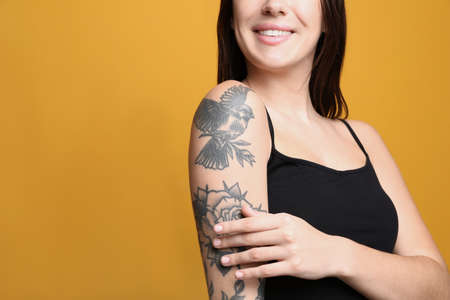 Beautiful woman with tattoos on arm against yellow background, closeup. Space for textの写真素材