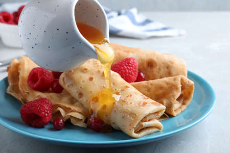 Pouring honey onto delicious crepes served with berries on light gray table, closeup