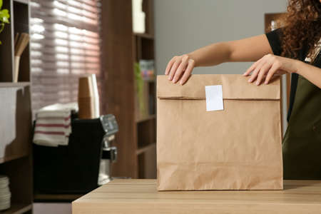 Worker with paper bag at counter in cafe, closeup. Space for textの写真素材