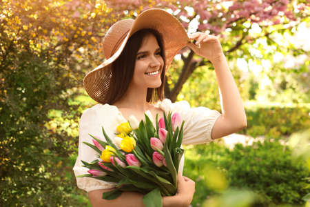 Beautiful young woman with bouquet of tulips in park on sunny day