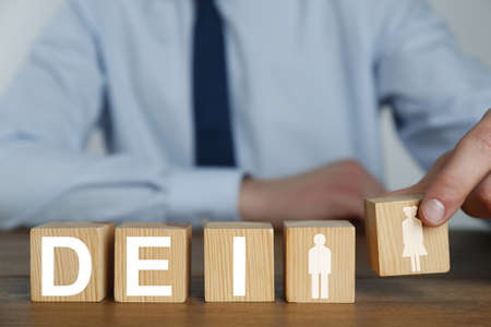 Concept of DEI - Diversity, Equality, Inclusion. Businessman and wooden cubes with letters and image of people on table, closeupの写真素材