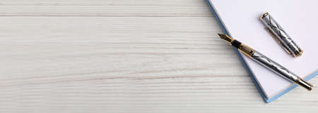 Beautiful fountain pen and notebook on white wooden table, top view with space for text. banner...