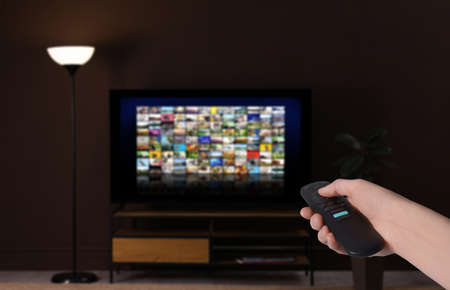 Woman with remote control changing channels while watching TV at home, closeupの写真素材