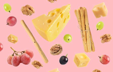 Cheese, breadsticks, grapes and walnuts falling against pale pink backgroundの写真素材
