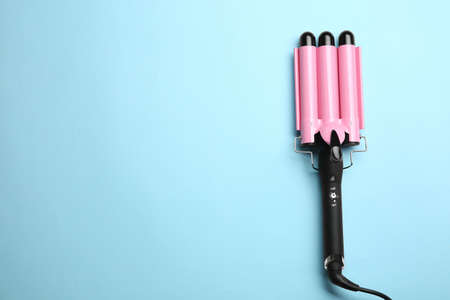Modern triple curling hair iron on light blue background, top view. Space for textの写真素材