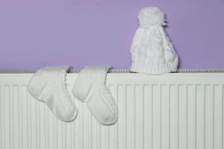 Knitted socks and hat on heating radiator near violet wallの写真素材