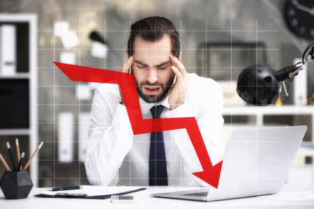 Stressed businessman at table in office and illustration of falling down chart. economy recession...
