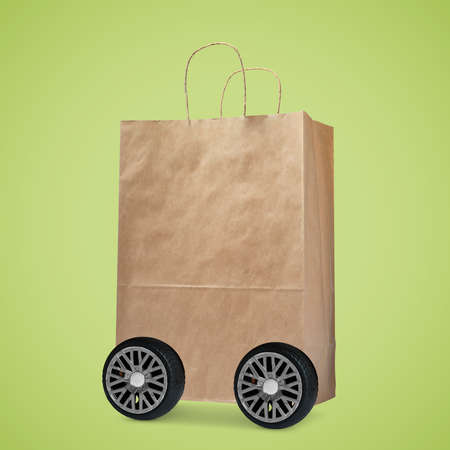 Paper shopping bag on wheels against yellowish green background. delivery service