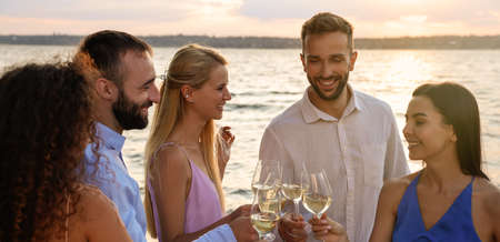 Friends with glasses of wine having fun near river at summer party. banner design