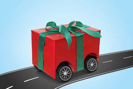 Gift box with wheels riding on asphalt road against light blue background. delivery serviceの写真素材