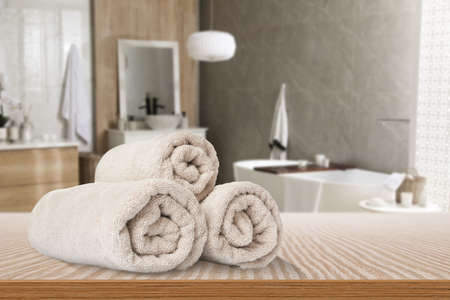 Rolled beige towels on wooden table in the bathroom. Space for text