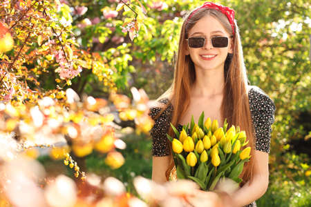 Beautiful teenage girl with bouquet of yellow tulips in park on sunny dayの写真素材