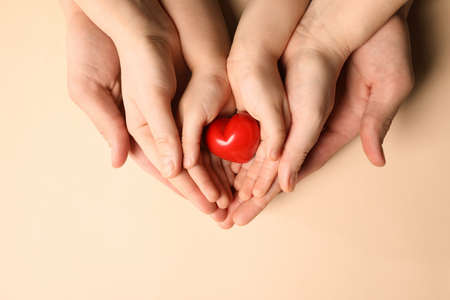 Parents and kid holding red heart in hands on beige background, top viewの写真素材