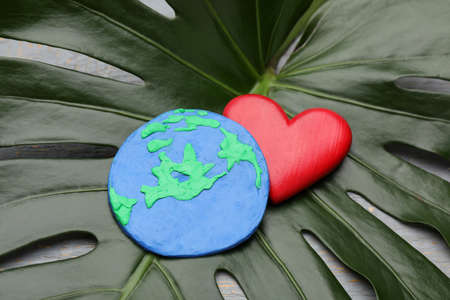 Happy Earth Day. Planet made of plastic and decorative heart on green leaf, closeupの写真素材