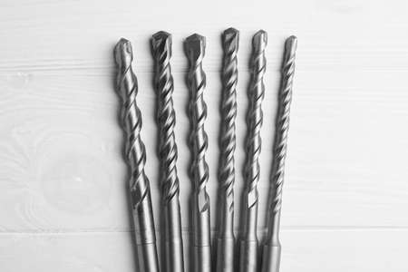 Different drill bits on white wooden table, flat lay