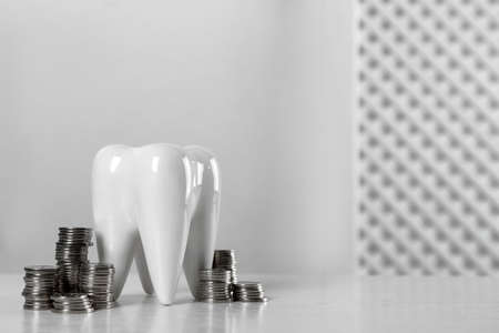 Ceramic model of tooth and coins on white table, space for text. Expensive treatmentの写真素材