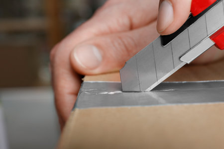 Man using utility knife to open parcel, closeupの写真素材