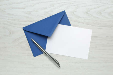 Envelope with blank paper card and pen on white wooden table, flat layの写真素材