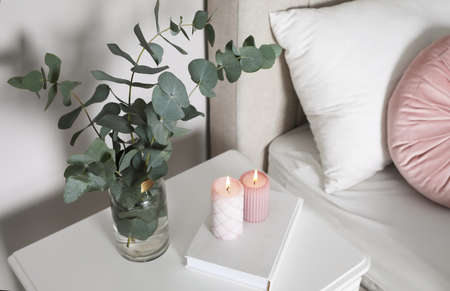 Vase with beautiful eucalyptus branches, book and candles on nightstand in bedroomの写真素材