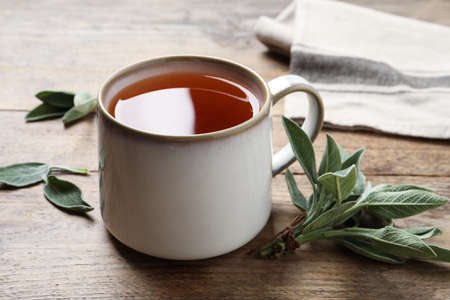 Cup of aromatic sage tea and fresh leaves on wooden tableの写真素材