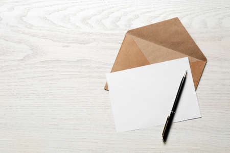 Envelope with blank paper card and pen on white wooden table, flat lay. Space for textの写真素材