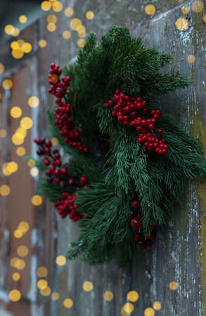 Beautiful Christmas wreath with red berries hanging on wooden wall outdoorsの写真素材