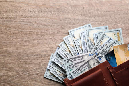 Many dollar banknotes with wallet and credit cards on wooden table, flat lay. Space for text