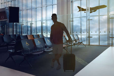 Young man with suitcase in waiting area at airport