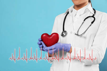 Closeup view of doctor with stethoscope holding red heart and illustration of cardiogram on turquoise backgroundの写真素材