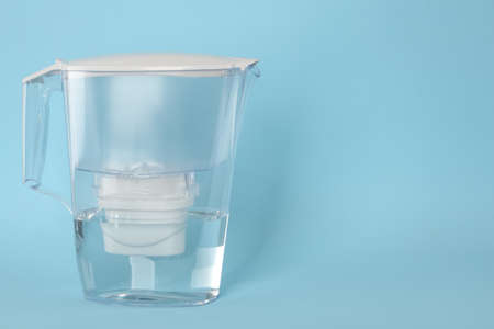 Filter jug with purified water on light blue background. Space for textの写真素材