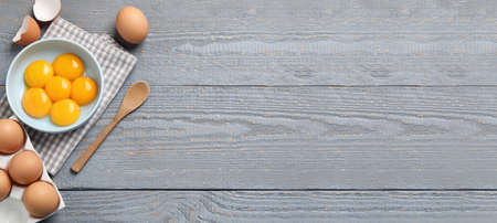 Fresh raw chicken eggs and spoon on gray wooden table, flat lay with space for text. banner design
