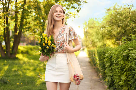 Beautiful teenage girl with bouquet of yellow tulips and apples in park on sunny day