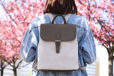 Young woman with backpack near blossoming sakura trees in park, back view