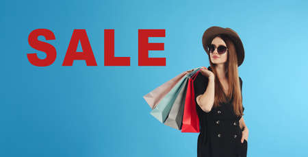 Beautiful young woman with paper shopping bags and word SALE on light blue background. banner designの写真素材