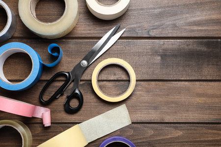 Rolls of adhesive tape and scissors on wooden background, flat lay. Space for textの写真素材
